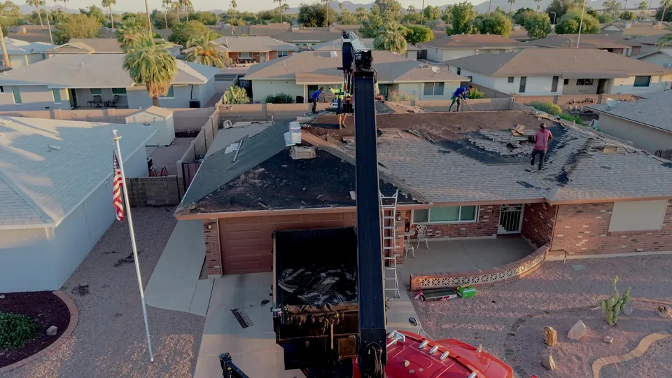 Crew tearing the old shingles off a roof, with a dump trailer in the driveway